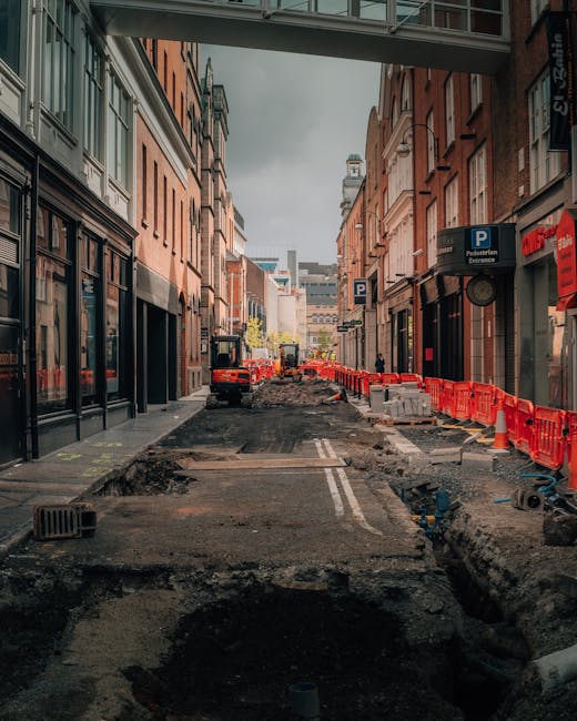 A red and white 'no entry' traffic sign mounted on a black pole stands on a narrow paved sidewalk beside a stone-paved street in Soho. The sidewalk is bordered by shopfront windows and entrances on th